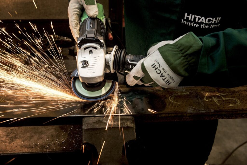 grinder-hitachi-power-tool-flexible-162534 Close-up of a skilled worker using a grinder with sparks flying in a metal workshop.